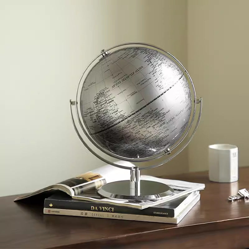 Decorative globe on a wooden surface with books and a mug in the background