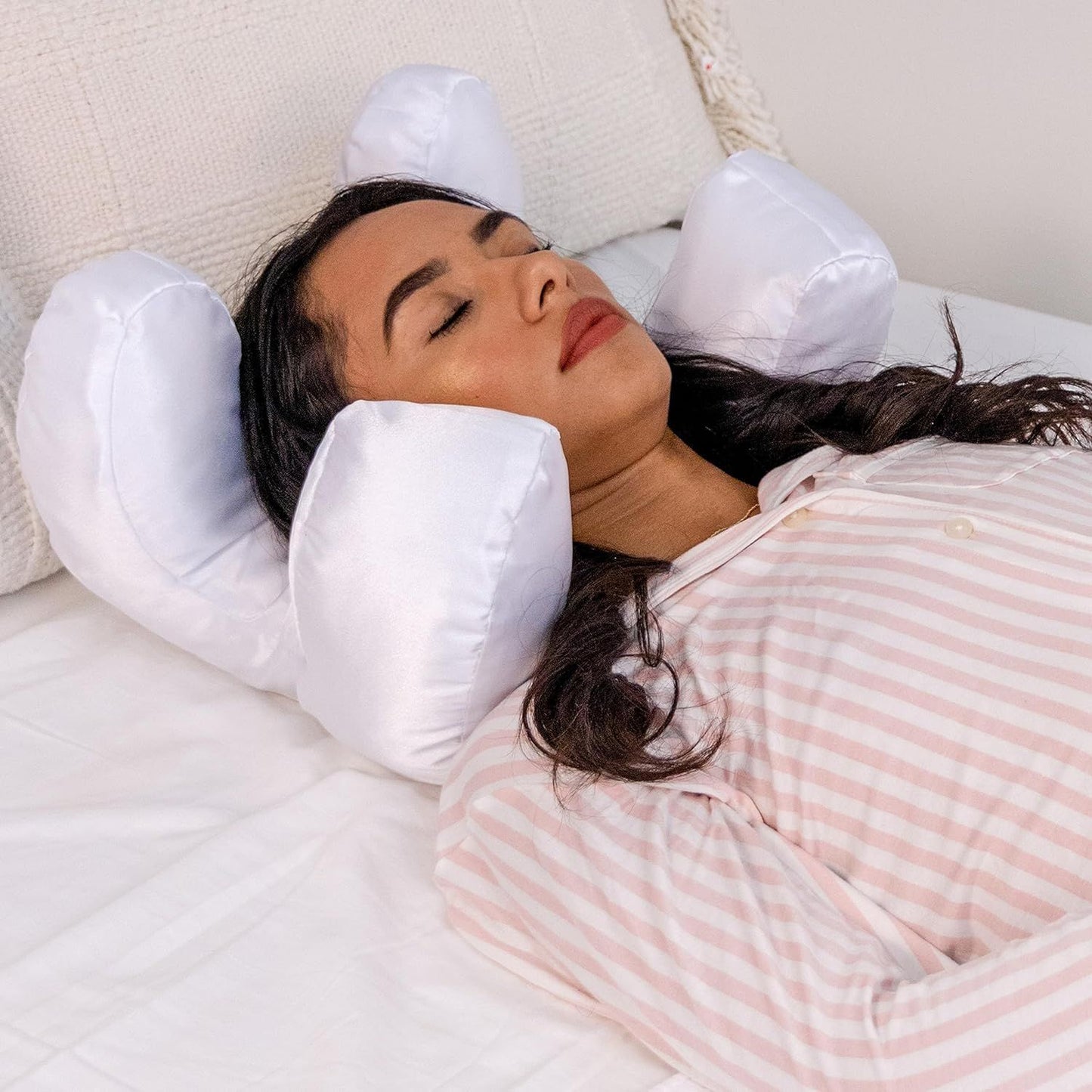 Woman lying on a bed with a white anti-wrinkle face-up pillow under her head.