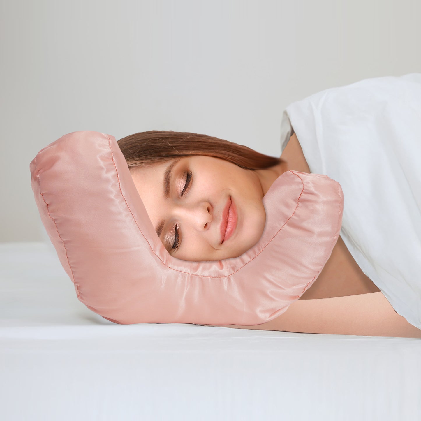 Woman using a pink anti-wrinkle face-up pillow on a white bed