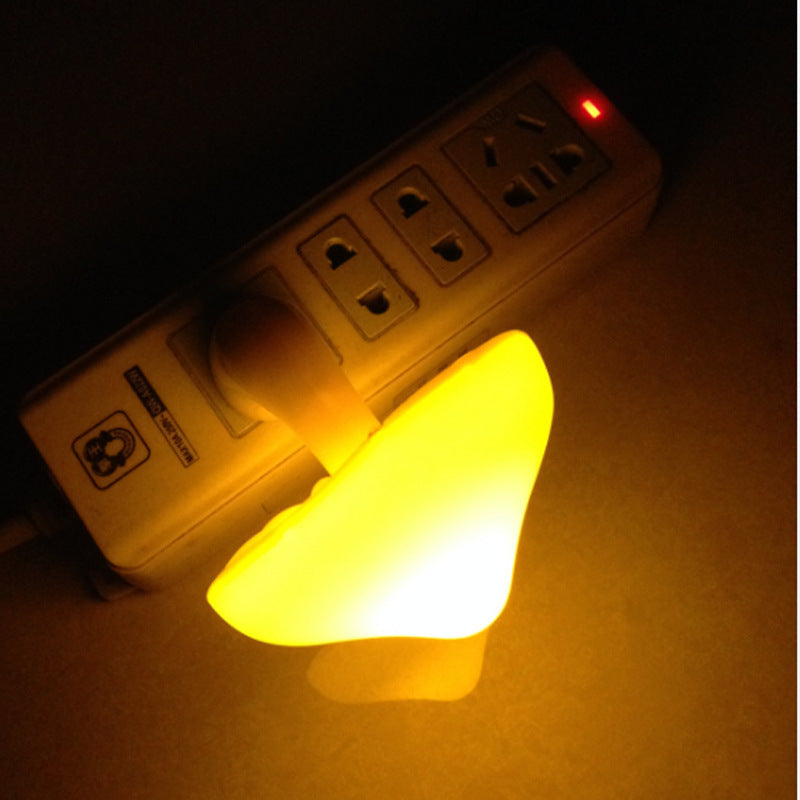 Small glowing mushroom shaped night light next to a power strip on a dark background