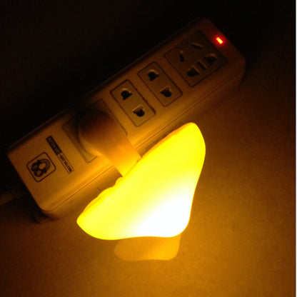 Small glowing mushroom shaped night light next to a power strip on a dark background