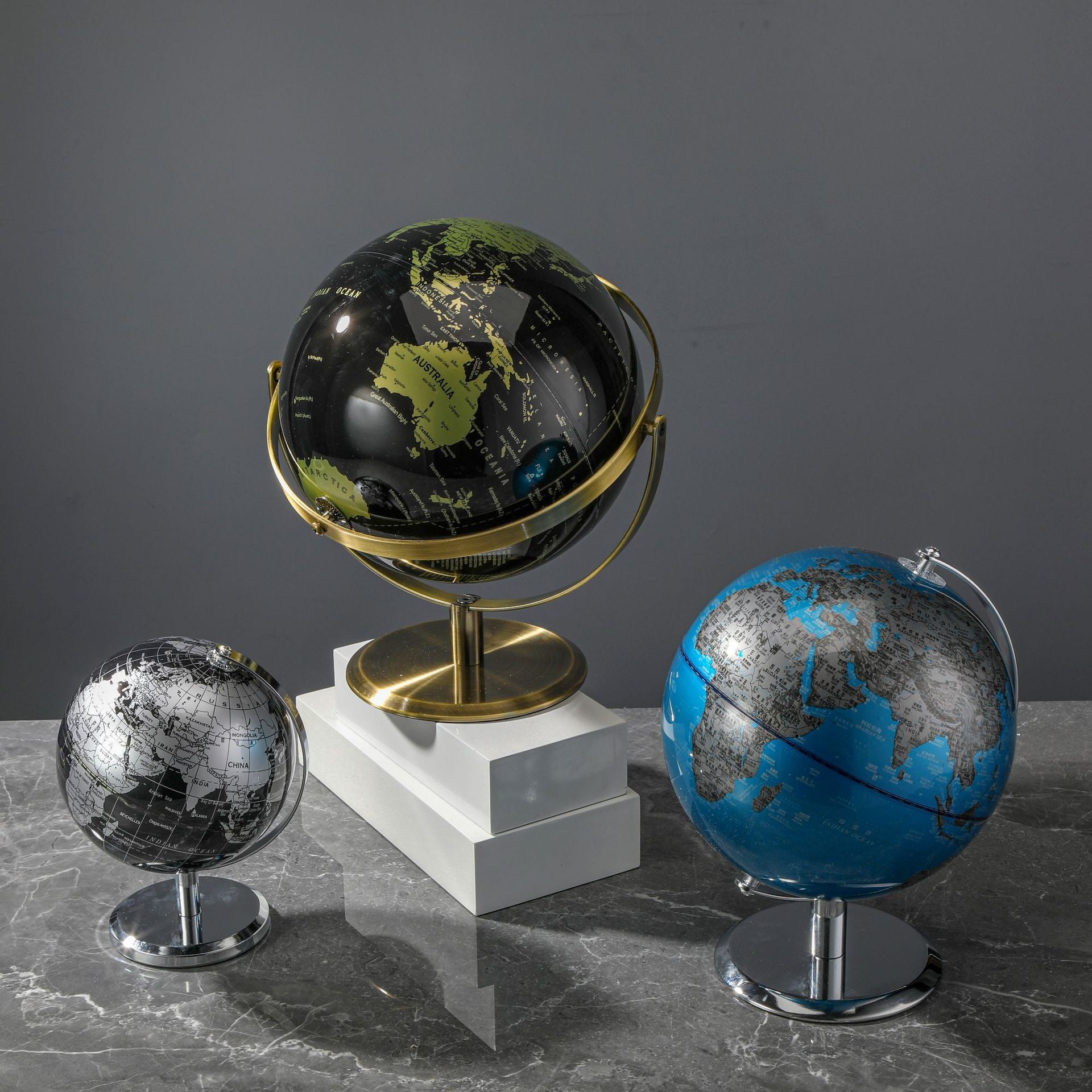 Three globes of different sizes on a gray surface with a dark gray background