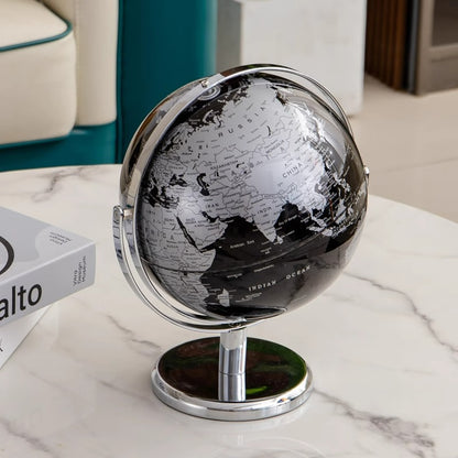 Black and silver world globe on a marble surface with a book in the background.