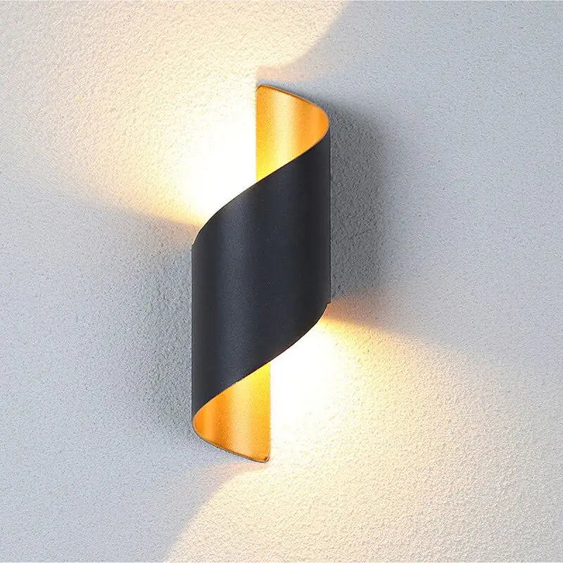Modern wall light fixture with black and gold design on a textured wall.