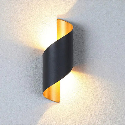 Modern wall light fixture with black and gold design on a textured wall.
